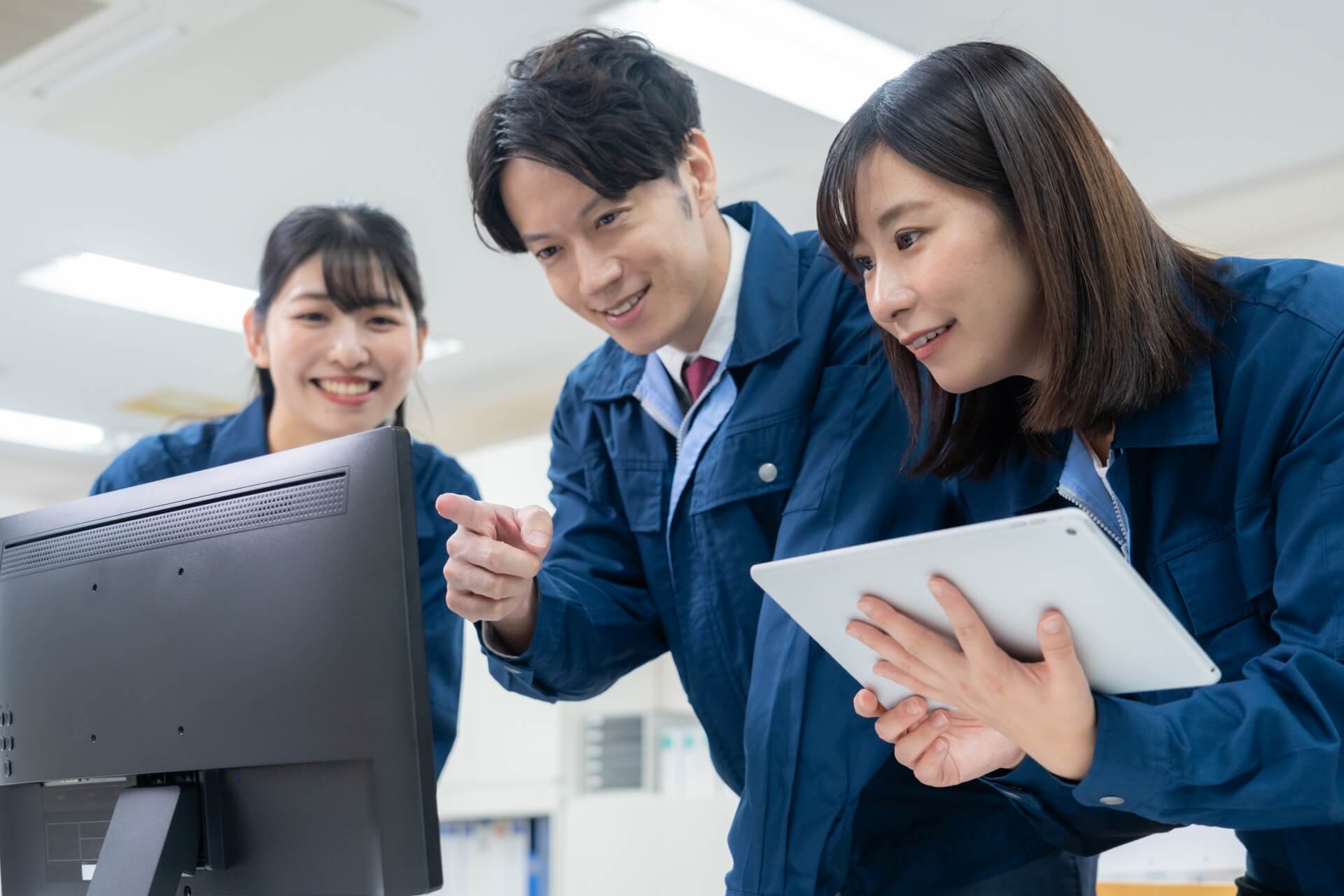 コンピュータ画面を指差す作業服の集団